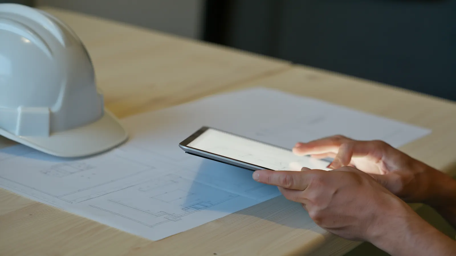 Hands holding a tablet over printed construction drawings